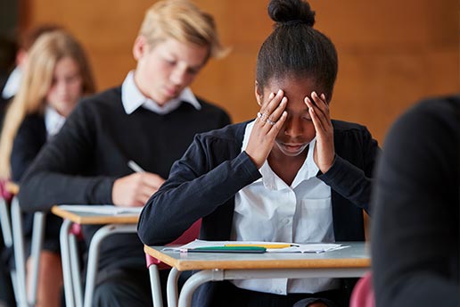 student with her head in her hands looking in dismay down at a test paper during an exam
