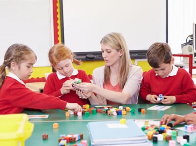 Primary children learning with blocks, being guided by a teacher