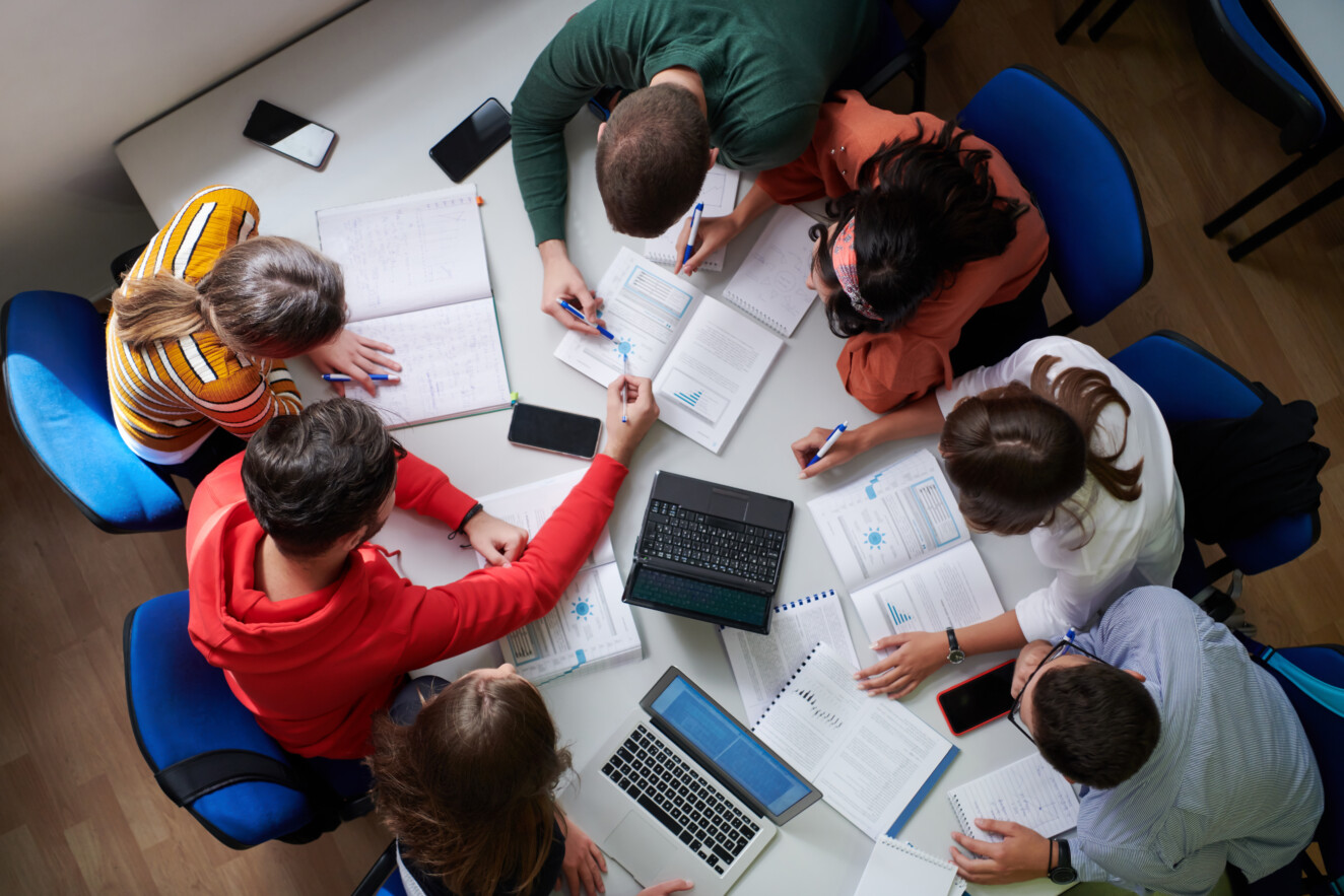 Top view of students sitting at a table studying and working on laptop
